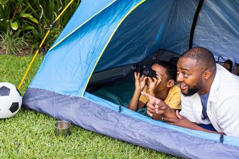 African american father and son camping in backyard pointing and looking through binoculars