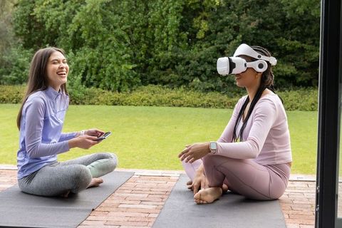 Diverse friends practicing yoga and exploring virtual reality together on backyard patio