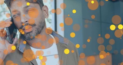 Indian man talking on smartphone at home wearing brown overshirt with orange bokeh lights