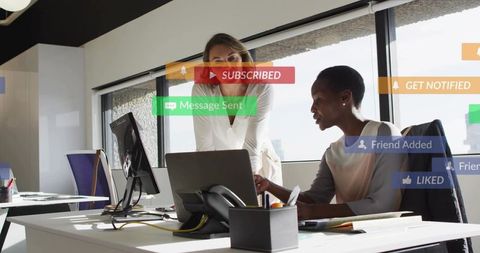 Two colleagues collaborating over laptop in modern office with social notifications overlay