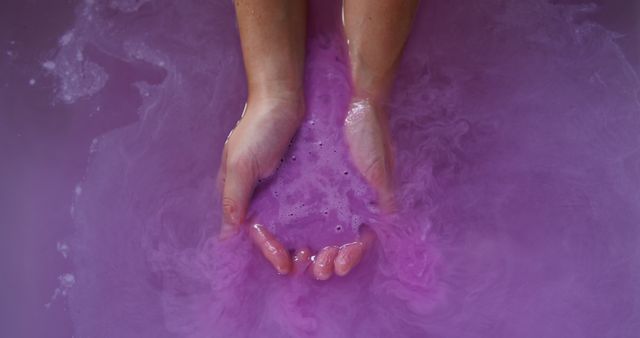 Hands are gently dipping into soothing purple water, creating a serene and tranquil atmosphere. This can be used for wellness and self-care promotions, beauty product advertisements, calm and relaxation themes, or spa-related content.