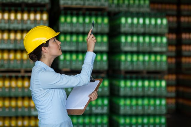 Attentive female factory worker maintaining record on clipboard in factory