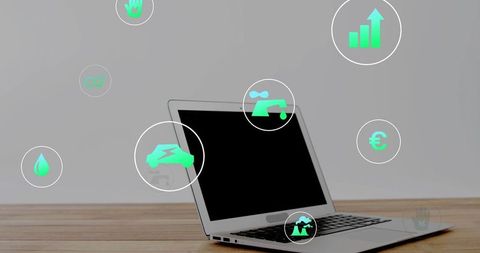 Silver laptop on wood desk showing green sustainability icons for business energy finance