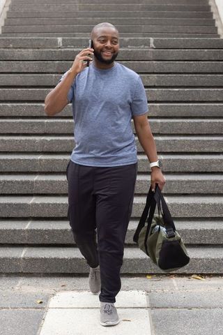 African american man walking down stairs talking on phone carrying gym duffel urban commute