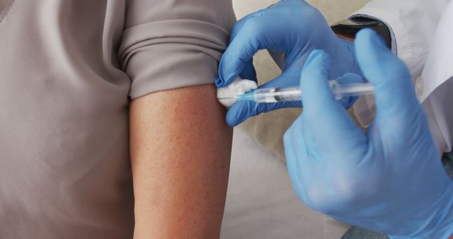 Healthcare professional wearing blue gloves administering vaccine in patient's arm. Useful for articles or marketing materials focused on vaccination campaigns, healthcare services, medical treatment procedures, public health initiatives, or clinic and hospital promotions.