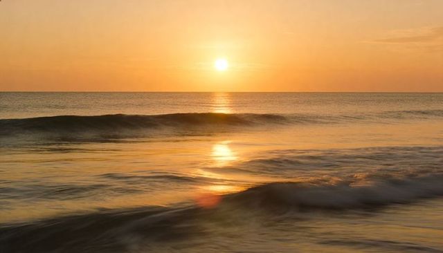 Rising sun casting golden path across calm ocean at dawn, tranquil minimalist seascape