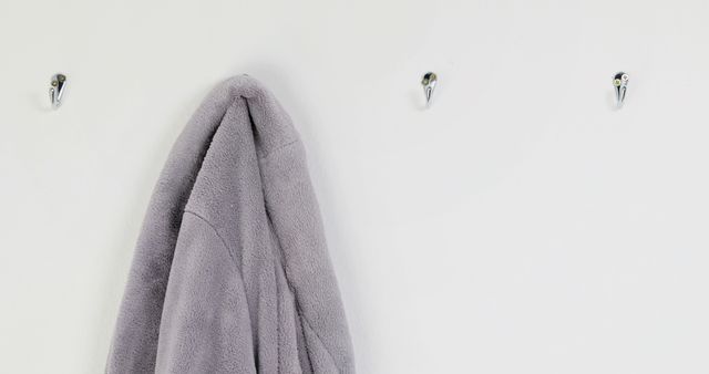 Gray towel hanging on metal hooks attached to white wall. Useful for topics related to home organization, minimalist living, bathroom decor, cleanliness, and interior design. Ideal for illustrating everyday scenes in a home setting focused on simplicity and functionality.