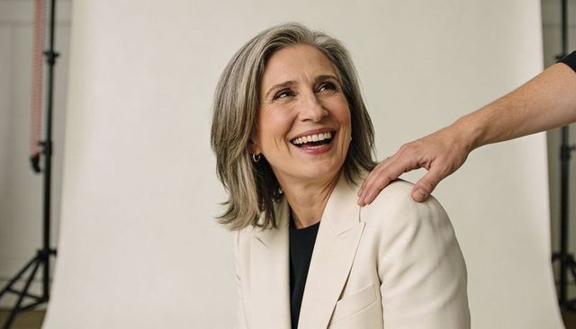 Smiling mature businesswoman receiving reassuring shoulder touch in light beige blazer