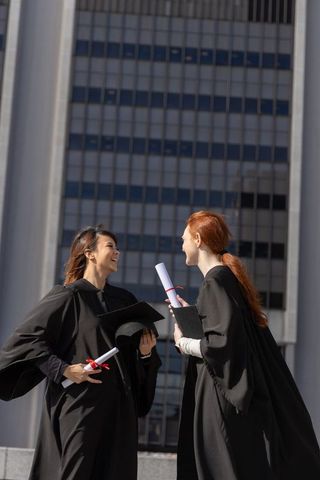 Diverse female graduates celebrating on urban plaza holding diplomas and mortarboards
