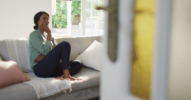 Image of thoughtful african american woman sitting on sofa. lifestyle and spending free time at home.
