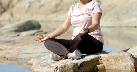 Woman Meditating on Rock by Water in Mountain Setting