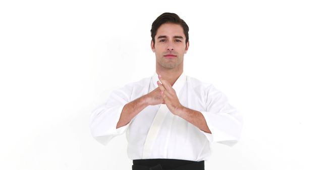A young Caucasian male martial artist is dressed in a traditional white karate gi, with copy space. He stands confidently with his hands together in front of him, demonstrating a respectful bow or starting position in martial arts.