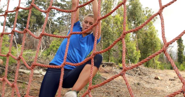 A young Caucasian woman is climbing a red rope net during an outdoor obstacle course challenge - Download Free Stock Photos Pikwizard.com