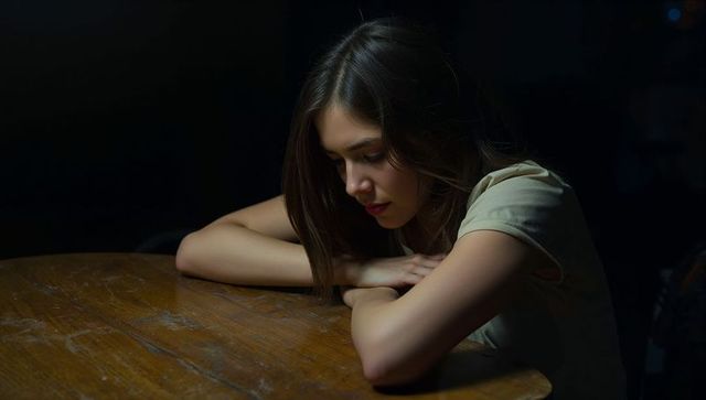 Pensive young asian woman leaning on wooden table in dim light, contemplative solitude