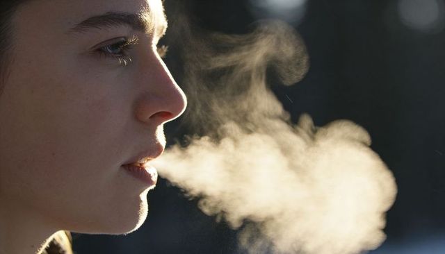 Teen female exhaling visible breath in cold winter air, closeup profile with warm vapor