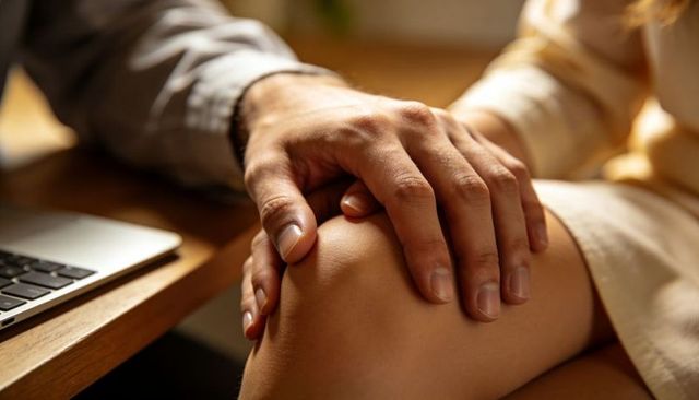 Man's hand resting on woman's knee beside laptop conveying intimacy and warmth