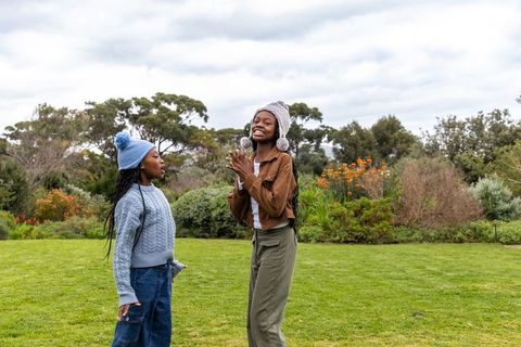 African american teen friends laughing and playing in park wearing knit pom-pom beanies