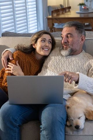 Middle-aged couple cuddling on sofa using laptop with sleeping golden retriever puppy