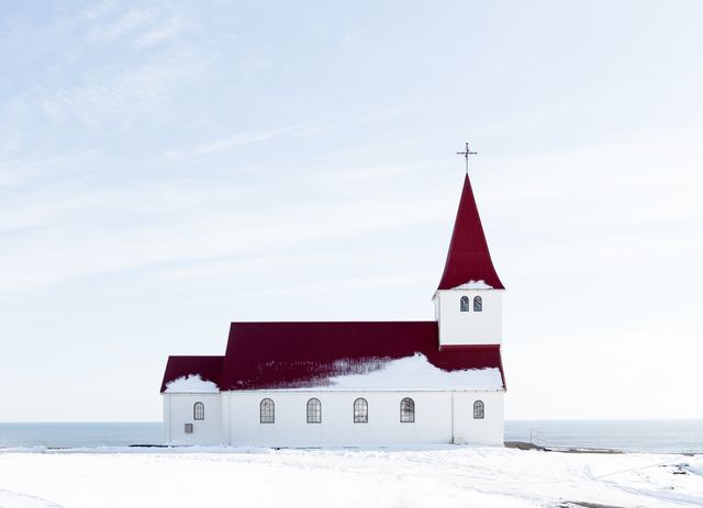 Detailed winter scene with a minimalist church featuring a striking red roof against white snow. Ideal for use in winter-themed projects, holiday greeting cards, religious publications, and architectural showcases.