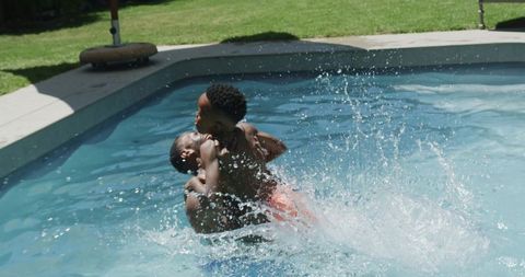 African american father lifting son while splashing in backyard pool summer family bonding