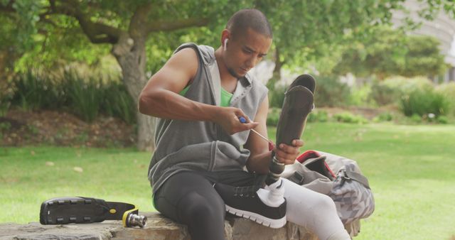 Man sitting on bench in park adjusting his prosthetic leg, showcasing adaptation and active lifestyle. Could be used for promoting outdoor activities, fitness, or inclusivity. Ideal for articles on overcoming physical challenges or motivational pieces.