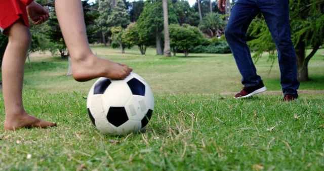 A child and an adult are playing soccer together in a grassy park, with copy space. Engaging in sports activities like this promotes physical health and strengthens family bonds.