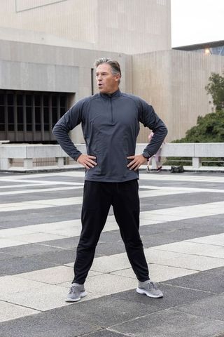 Man pausing with hands on hips on patterned urban plaza, outdoor fitness and stamina
