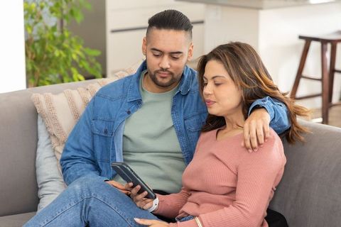 Mid-adult couple relaxing on sofa using smartphone, cozy home moment