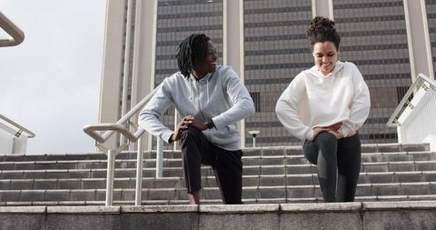 Multicultural friends doing lunges on urban steps in front of office tower, outdoor workout