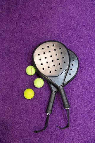 Crossing black padel paddles with three yellow balls on vibrant purple court texture