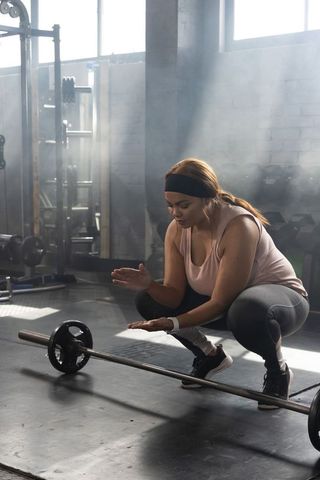 African american woman preparing deadlift, squatting over barbell in gritty sunlit gym