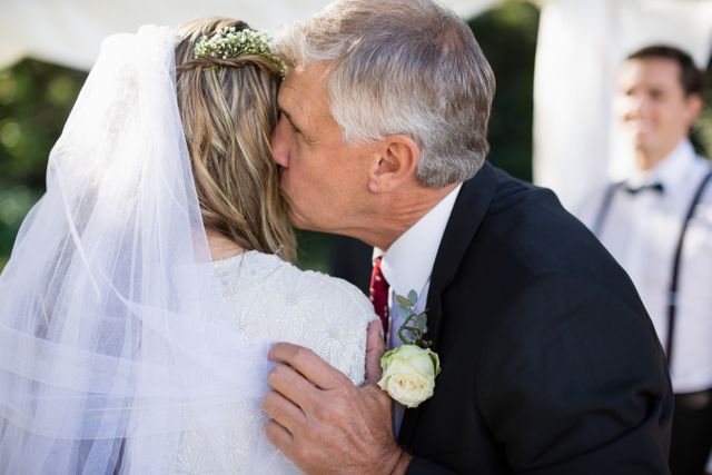 Father kissing his daughter on her wedding day, showing affection and love during the ceremony. Suitable for use in wedding-related content, family celebrations, emotional moments, and father-daughter relationships.