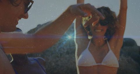 Couple celebrating at rocky beach with woman raising arms in white bikini holding mirror