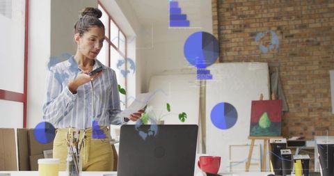 Artist speaking into smartphone while reviewing papers in bright brick-walled loft studio