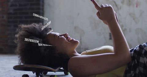 Modern tech-savvy woman with smartphone skateboarding indoors