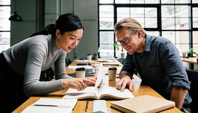 Colleagues collaborating over open book in modern coworking office, studying together