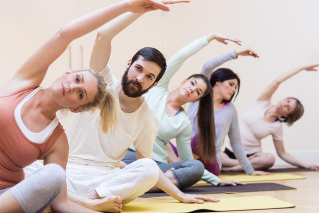 Group of people engaging in stretching exercises in a fitness studio. Ideal for promoting fitness classes, wellness programs, and healthy lifestyle campaigns. Useful for illustrating group workouts, flexibility training, and community fitness activities.