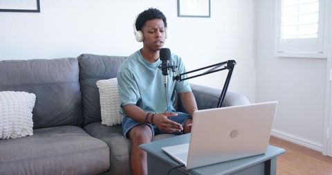 Young man recording podcast from home studio with laptop, condenser mic and headphones