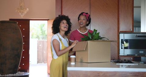 Diverse female couple unpacking moving box in modern home