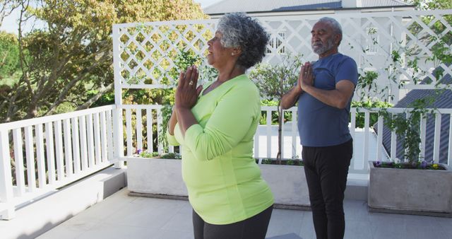Image of relaxed african american senior couple practicing yoga on patio. active and healthy retirement lifestyle at home and garden.