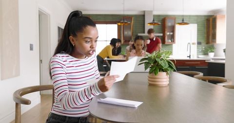 African American woman reading letter at kitchen island reacting while family gathers