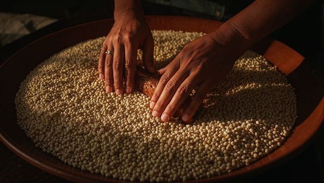 Hands rolling and pressing light grains on wooden tray for artisanal food preparation