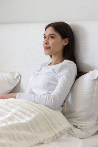 Serene woman relaxing in white minimalist bedroom with soft natural light and cozy blanket