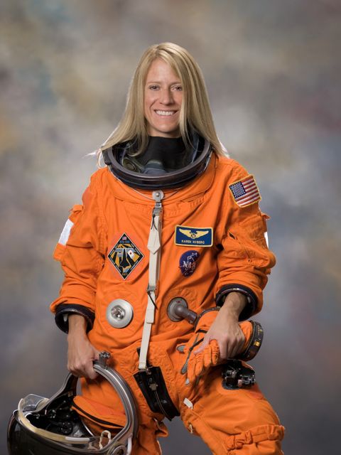 Karen Nyberg, a NASA astronaut, poses confidently in her orange spacesuit, holding a helmet in her right hand. This image, taken in 2007, is ideal for articles and educational materials related to space, science, and exploration. Perfect for promoting STEM awareness and inspiring future astronauts.