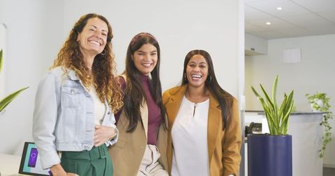 Diverse female coworkers laughing in modern reception wearing blazers and denim jacket