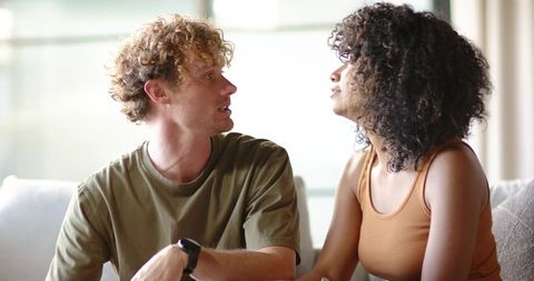 Young couple sharing quiet conversation on sunlit sofa at home, relaxed intimate moment