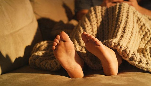 Bare feet relaxing on chunky knit throw draped over sofa under warm lamp glow