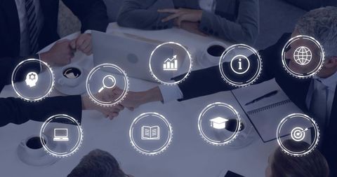 Businesspeople shaking hands over meeting table with digital icons representing partnership
