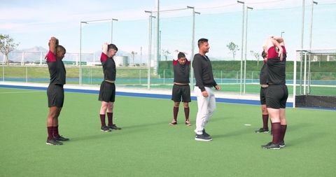 Male athletes stretching exercises with coach on soccer field