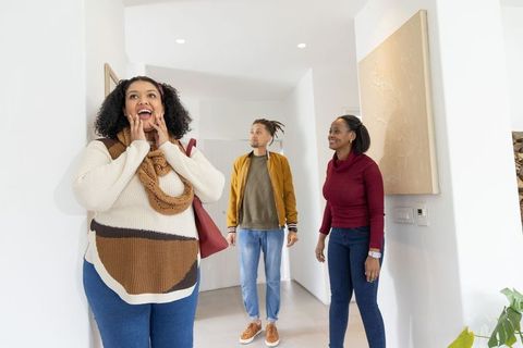 Multicultural friends touring modern home entryway, reacting with surprise and joy